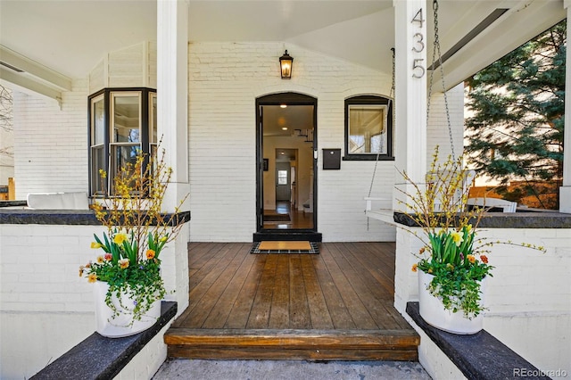 doorway to property featuring brick siding and covered porch
