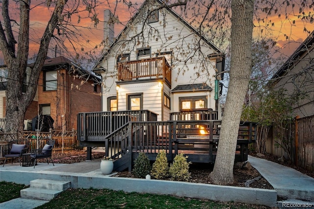 back of property at dusk featuring fence, a deck, and a balcony