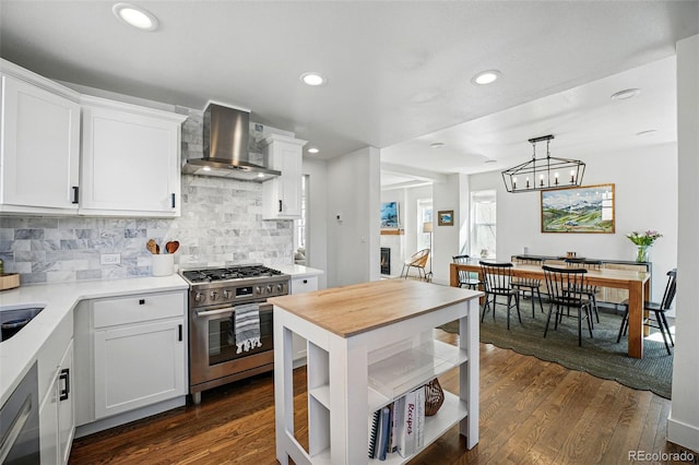 kitchen with wall chimney range hood, light countertops, dark wood-type flooring, decorative backsplash, and stainless steel range with gas cooktop