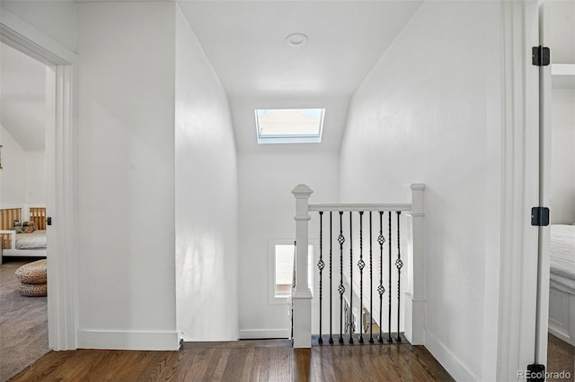 corridor featuring an upstairs landing, dark wood-style flooring, baseboards, and lofted ceiling with skylight