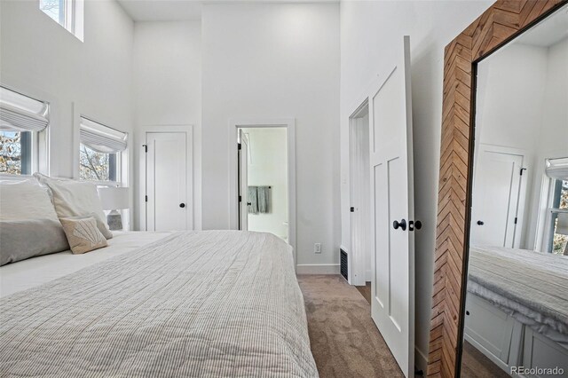 bedroom featuring ensuite bathroom, a towering ceiling, baseboards, and carpet floors