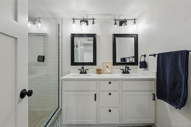 bathroom featuring double vanity, a tile shower, and a sink