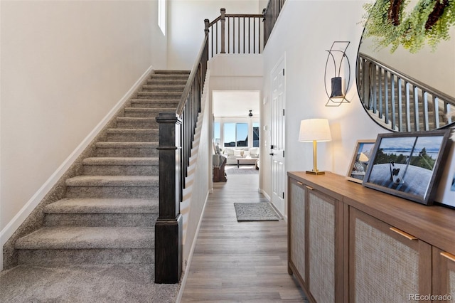 stairs featuring a high ceiling, baseboards, and wood finished floors