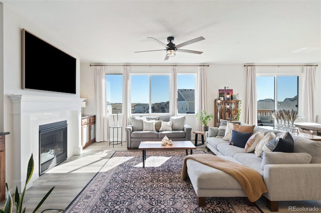 living room featuring a ceiling fan, a glass covered fireplace, and light wood-style flooring