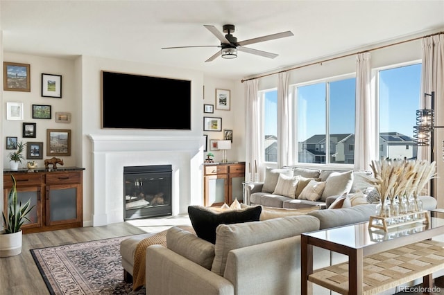 living area with a glass covered fireplace, ceiling fan, and light wood-style flooring