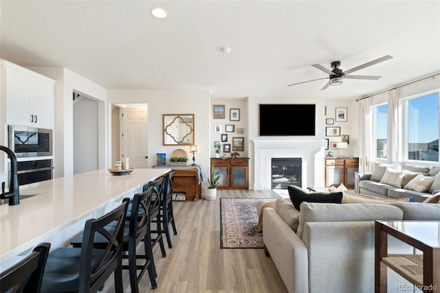 living area featuring a ceiling fan, a glass covered fireplace, light wood-style flooring, and recessed lighting