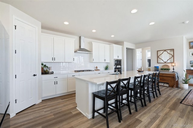 kitchen with stainless steel appliances, white cabinetry, a sink, wall chimney range hood, and a large island with sink