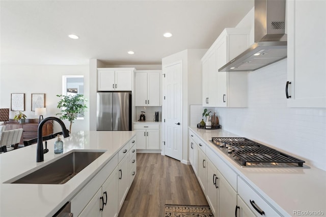 kitchen featuring wall chimney exhaust hood, appliances with stainless steel finishes, white cabinets, and a sink