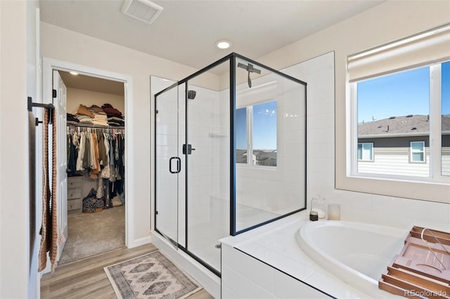 bathroom featuring wood finished floors, visible vents, a bath, a stall shower, and a walk in closet