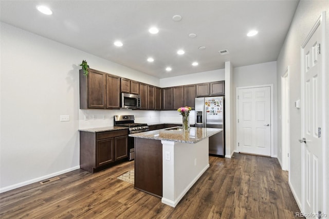 19221 E 65th Ave, Denver, CO 80249 - kitchen with appliances with stainless steel finishes, dark brown cabinets, dark wood-type flooring, a center island with sink, and light stone counters