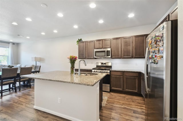 19221 E 65th Ave, Denver, CO 80249 - kitchen featuring stainless steel appliances, dark wood-style flooring, light stone countertops, a kitchen island with sink, and recessed lighting