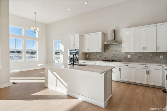 kitchen featuring wall chimney exhaust hood, light hardwood / wood-style floors, white cabinetry, and sink