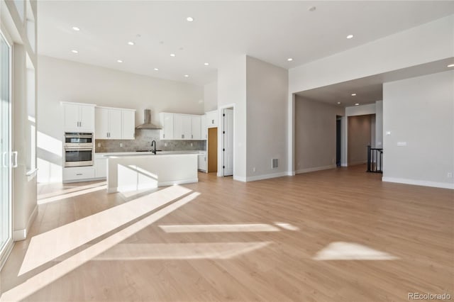 kitchen featuring sink, light hardwood / wood-style flooring, double oven, an island with sink, and white cabinets