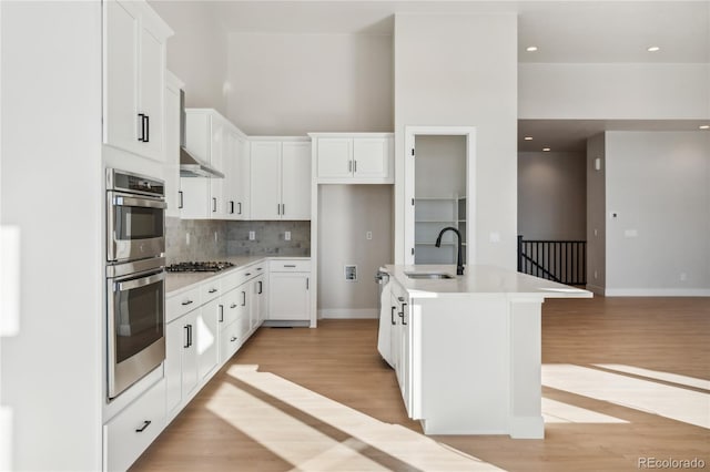 kitchen with sink, an island with sink, light hardwood / wood-style floors, white cabinetry, and stainless steel appliances