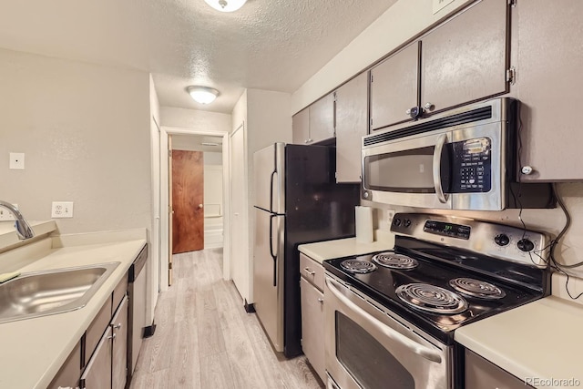 kitchen with appliances with stainless steel finishes, a textured ceiling, sink, and light wood-type flooring