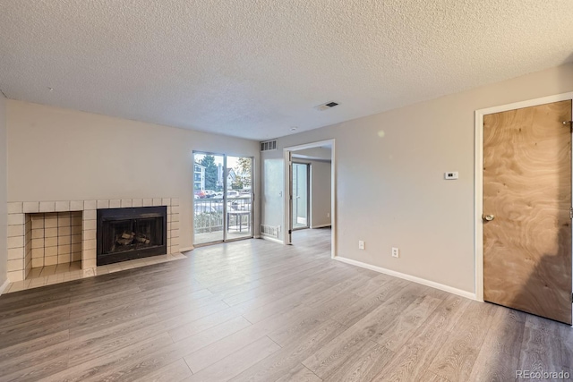 unfurnished living room with a textured ceiling, a tiled fireplace, and light hardwood / wood-style floors