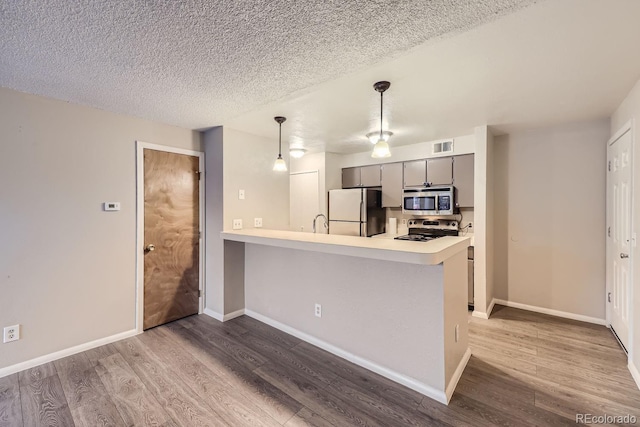 kitchen featuring kitchen peninsula, hardwood / wood-style floors, stainless steel appliances, decorative light fixtures, and gray cabinets