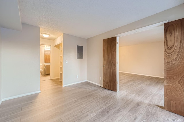 spare room with a textured ceiling, electric panel, and light wood-type flooring