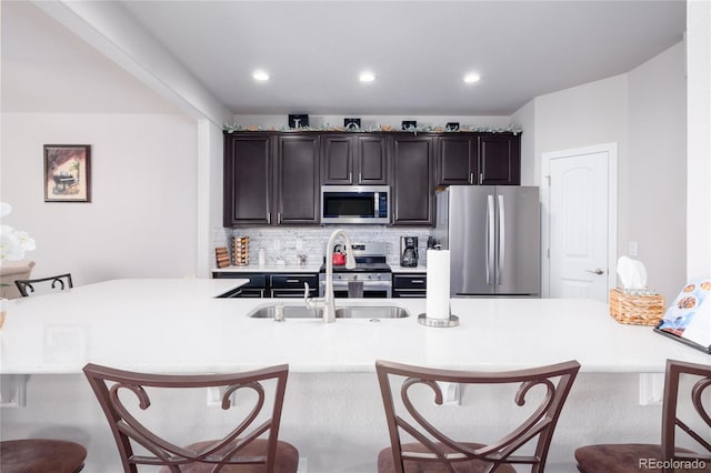 kitchen featuring stainless steel appliances, a sink, a kitchen breakfast bar, light countertops, and decorative backsplash