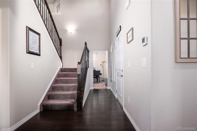 hall with a towering ceiling, dark wood-style floors, stairs, and baseboards