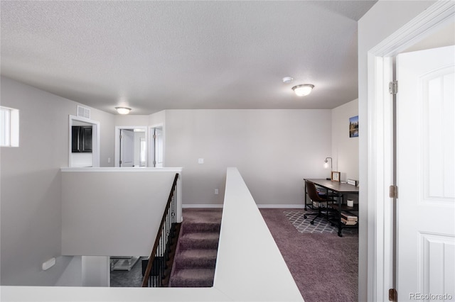 interior space featuring a textured ceiling, dark carpet, an upstairs landing, and baseboards