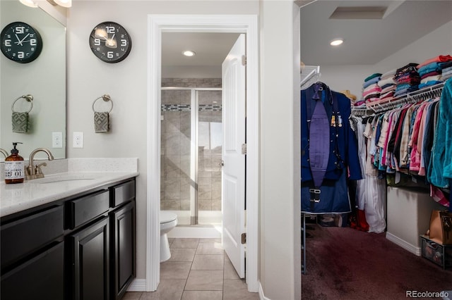 bathroom featuring a walk in closet, toilet, a shower stall, vanity, and tile patterned flooring