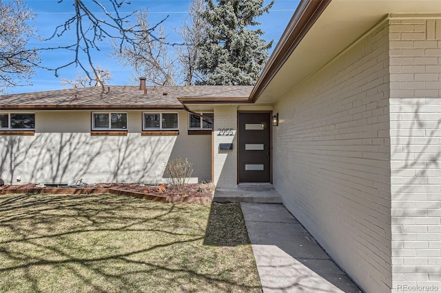 entrance to property featuring a yard, brick siding, and a shingled roof