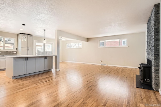 unfurnished living room featuring baseboards, visible vents, light wood finished floors, and a textured ceiling