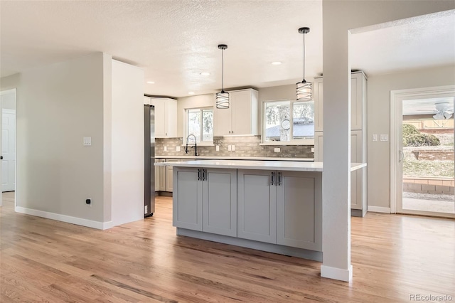 kitchen featuring gray cabinets, backsplash, freestanding refrigerator, light wood-style floors, and light countertops