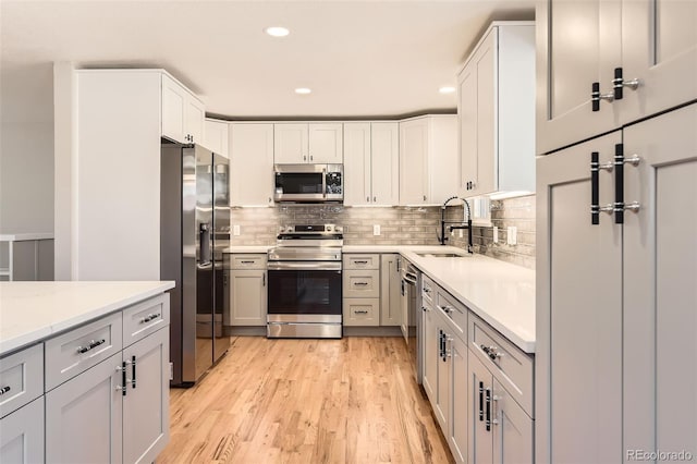 kitchen featuring backsplash, light wood-style flooring, stainless steel appliances, and a sink