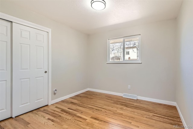 unfurnished bedroom with light wood-style flooring, baseboards, visible vents, and a closet