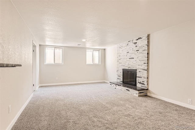 unfurnished living room featuring a textured ceiling, a fireplace, baseboards, and carpet