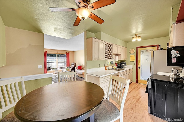 dining area with ceiling fan, a textured ceiling, sink, and light wood-type flooring