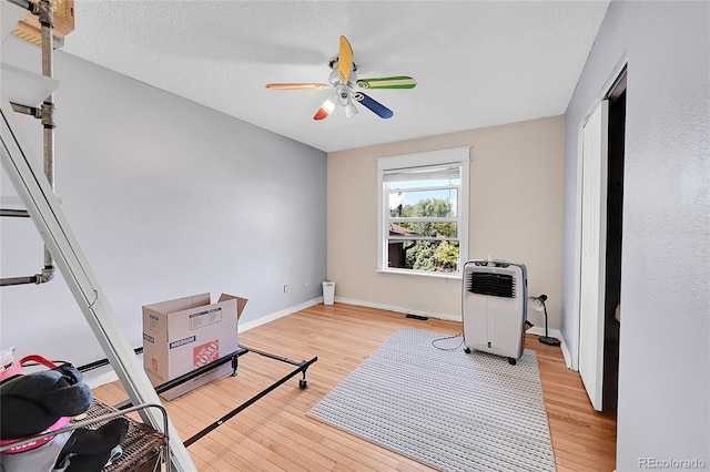 workout area with a textured ceiling, light hardwood / wood-style floors, and ceiling fan