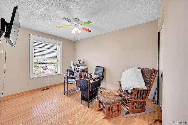 office area with a textured ceiling, light wood-type flooring, and ceiling fan