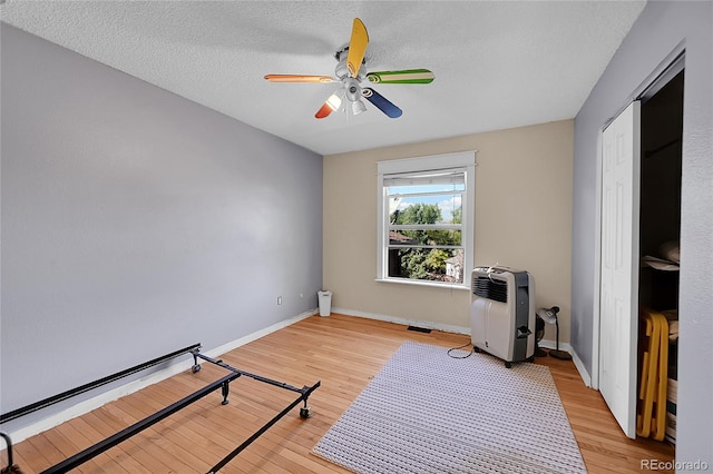 exercise area with light hardwood / wood-style floors, a textured ceiling, and ceiling fan