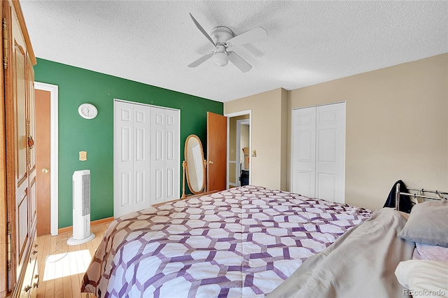 bedroom with hardwood / wood-style floors, two closets, a textured ceiling, and ceiling fan