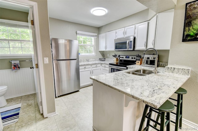 8022 S Columbine Ct, Centennial, CO 80122 - kitchen with appliances with stainless steel finishes, a peninsula, light stone countertops, white cabinets, and a breakfast bar