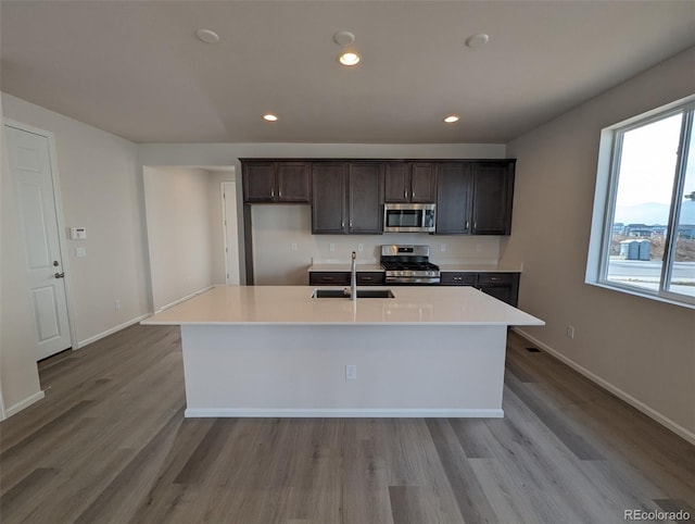 kitchen featuring a kitchen island with sink, sink, stainless steel appliances, and light wood-type flooring