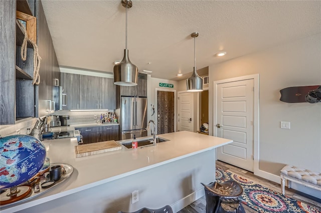 kitchen with hardwood / wood-style floors, sink, high end fridge, decorative light fixtures, and kitchen peninsula