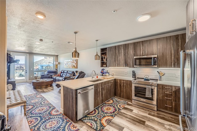 kitchen with sink, kitchen peninsula, appliances with stainless steel finishes, and light wood-type flooring