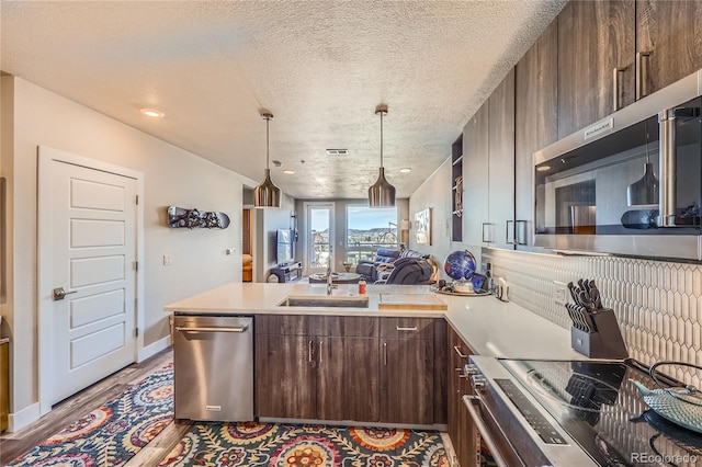 kitchen with appliances with stainless steel finishes, dark brown cabinets, wood-type flooring, a textured ceiling, and sink