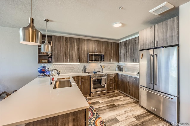 kitchen featuring appliances with stainless steel finishes, sink, decorative light fixtures, kitchen peninsula, and dark brown cabinets