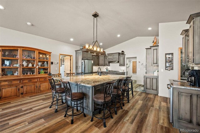 kitchen featuring light stone counters, lofted ceiling, stainless steel fridge, dark wood-type flooring, and a spacious island