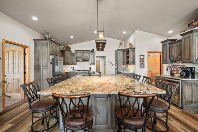 kitchen featuring lofted ceiling, beverage cooler, a large island with sink, a kitchen breakfast bar, and dark hardwood / wood-style flooring