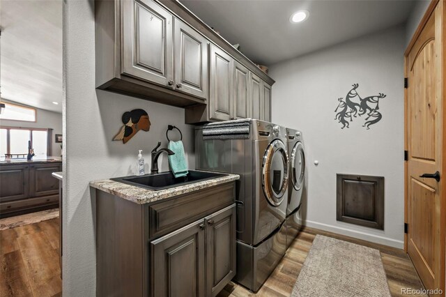 laundry area featuring independent washer and dryer, sink, light hardwood / wood-style floors, and cabinets