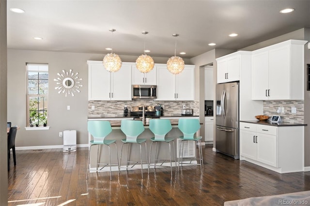 15194 W Washburn Ave, Lakewood, CO 80228 - kitchen featuring appliances with stainless steel finishes, decorative backsplash, a breakfast bar, dark wood-style floors, and a kitchen island with sink