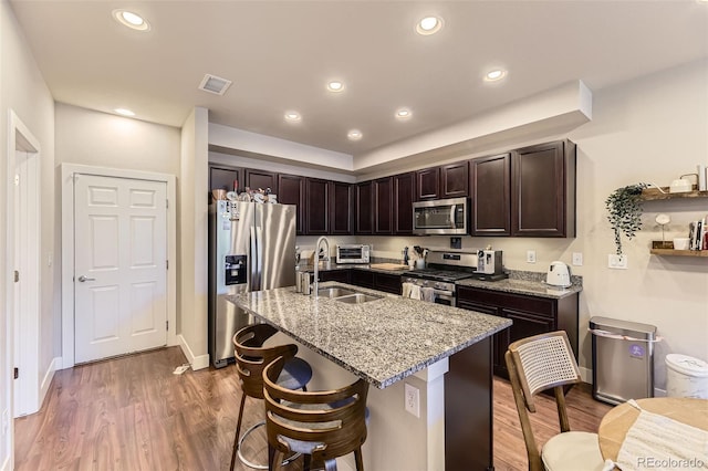 16057 E 47th Pl, Denver, CO 80239 - kitchen featuring stainless steel appliances, light stone counters, dark brown cabinets, a sink, and wood finished floors