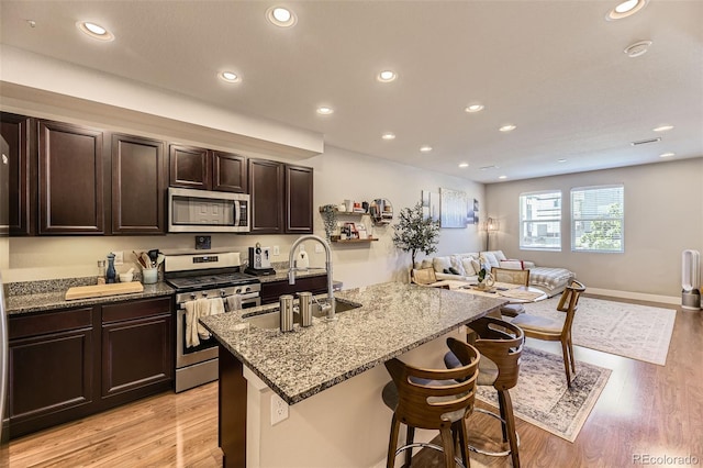 16057 E 47th Pl, Denver, CO 80239 - kitchen featuring appliances with stainless steel finishes, a sink, light stone counters, a kitchen breakfast bar, and light wood finished floors