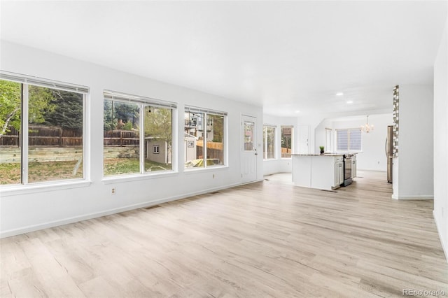 524 Rider Ridge Dr, Longmont, CO 80504 - unfurnished living room with light wood-style floors, a healthy amount of sunlight, and an inviting chandelier